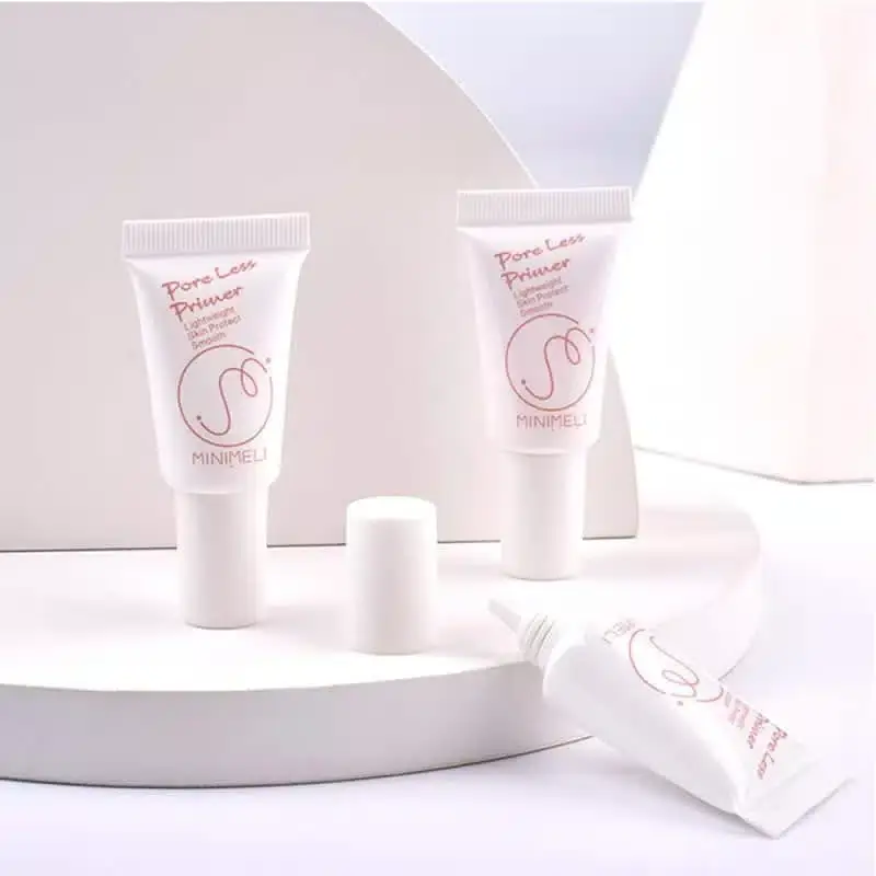 A hand gently holds the Minimeli Pore Invisible Primer 6ml white tube with pink cap. - thumbnail